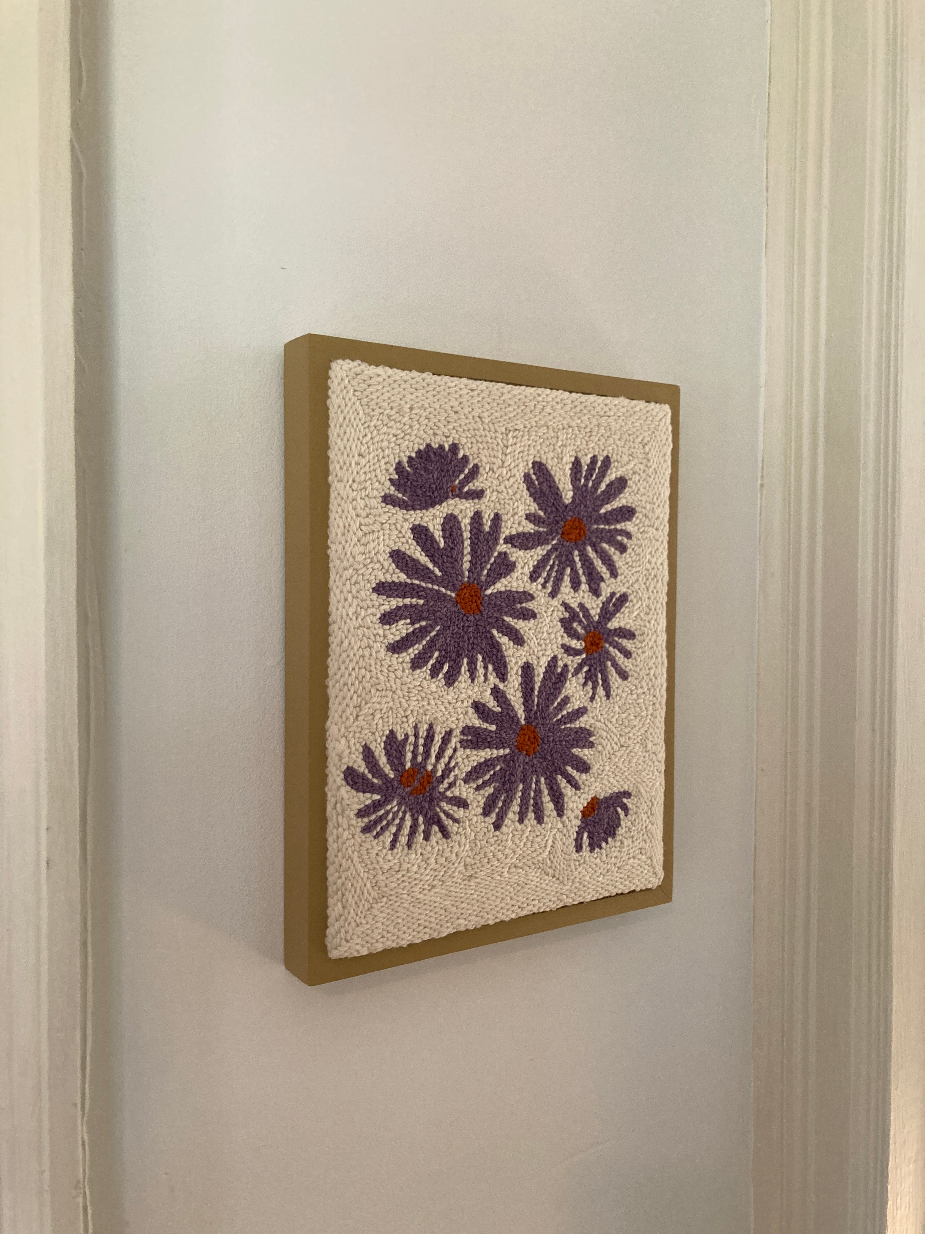 Embroidered punch needle wall art pattern of blooming purple aster patterns on a creamy background and framed